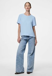 Ljusblå topp med korta ärmar och en texturerad yta, kombinerad med löst sittande ljusblå jeans och svarta klackskor.