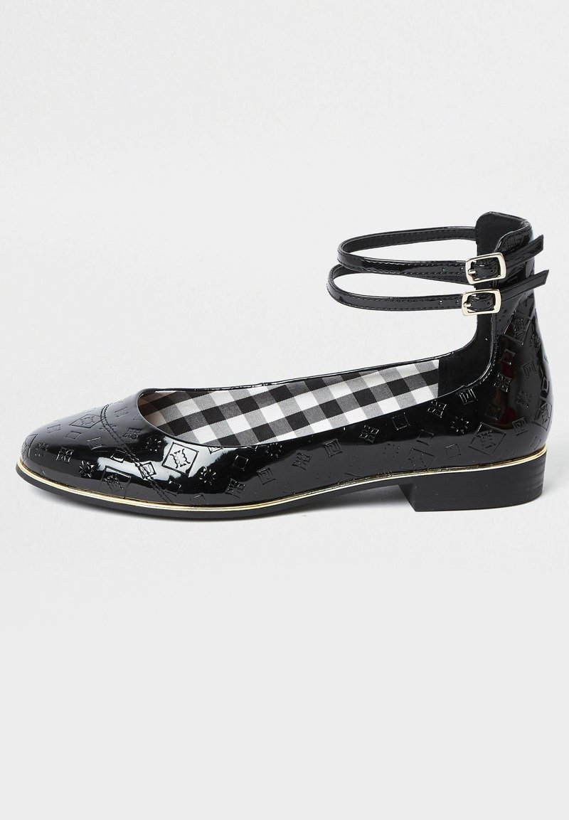 Chaussure plate en cuir verni noir avec motifs embossés, doubles brides autour de la cheville avec boucles argentées, talon bas et doublure intérieure à carreaux noirs et blancs.
