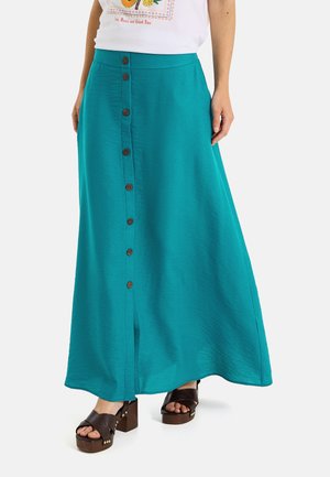 Falda larga estilo línea A en color verde azulado con botones marrones delanteros, combinada con sandalias negras de plataforma y una camiseta blanca con estampado.
