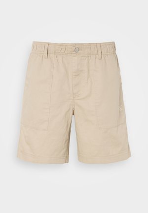 Beige cotton shorts with elastic waist, front button, and two side pockets. Features subtle stitching and a small logo on the side.
