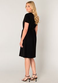 Zwarte jurk met korte mouwen, een aangesloten lijfje en een geplooide rok. Gladde stof, een getailleerde taille en enkellaarsjes met een puntige neus.