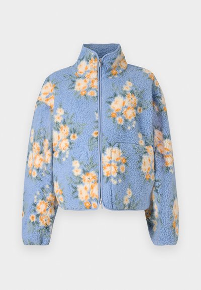 Sinine fliisjope oranži ja valge lillemustriga, millel on tõmblukk, kõrge krae ja kaks esimest taskut. Pehme tekstuur.