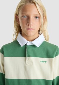Groene en crèmekleurige gestreepte polo met witte kraag, voorzien van een klein geborduurd logo. Zachte textuur, knoopsluiting bij de hals.