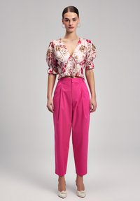 Floral print cropped blouse with puffed sleeves; paired with high-waisted, pleated pink trousers. Model wears nude shoes with a bow detail.