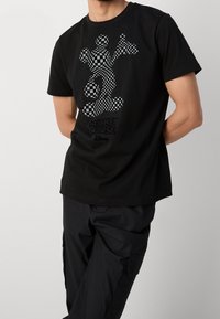 Černé bavlněné tričko s kostkovaným grafickým motivem Mickey Mouse na přední straně. Kulatý výstřih, krátké rukávy a pohodlný střih.