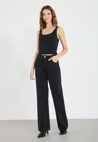 Svart, kort tanktopp med frontknapper, kombinert med høy midje, svarte vidbukser og spisse, svarte hæler. Glatt tekstur, enkelt design.