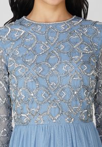 Vestido azul claro con intrincados bordados y perlas de plata, mangas largas y transparentes, y una falda de tul acampanada.