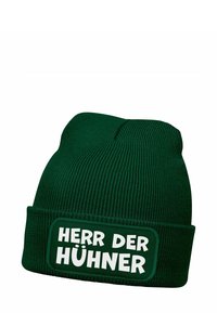 Green knitted beanie with ribbed texture. Features a rectangular patch with the text “HERR DER HÜHNER” in bold white letters.