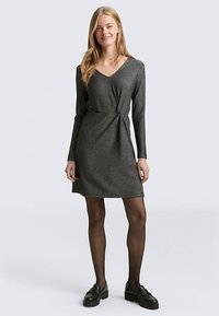 Gebreide, donkergrijze jurk met een V-hals, lange mouwen, knoopdetail in de taille en een rechte rok, gecombineerd met zwarte schoenen en panty's.