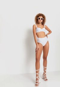 Vitt bikinitält med en strukturerad, axelbandslös topp och högmidjade underdelar. Kombinerat med vita remklackar och stora solglasögon.