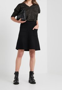 Mustat hameet, joissa on kaksi etutaskua, yhdistettynä kiiltävään mustaan lyhythihaiseen paitaan. Asusteina musta clutch ja massiiviset mustat saappaat.