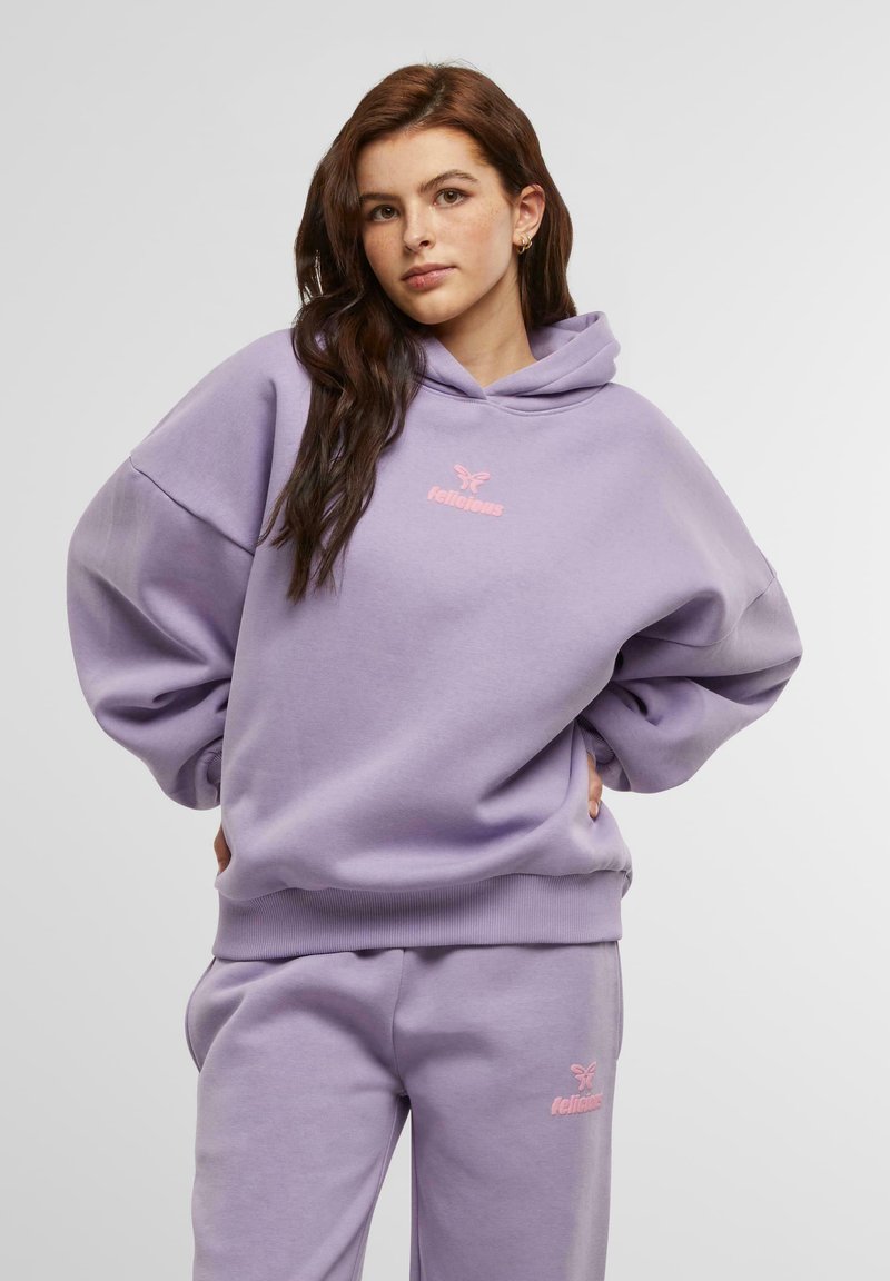 Lilla hettegenser med en avslappet passform, med en rosa logo. Myk tekstur og ribbet kant, kombinert med matchende joggebukser.