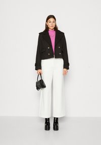 Czarna krótka marynarka dwurzędowa z złotymi guzikami, połączona z różowym golfem, białymi spodniami o szerokich nogawkach i czarną torebką.