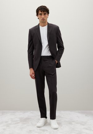 Traje de tela gris oscuro con un ajuste entallado, emparejado con una camiseta blanca de cuello redondo y zapatillas blancas. Textura suave, detalles mínimos.