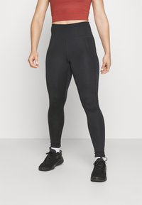 Høytlivde svarte leggings laget av elastisk materiale, med en jevn tekstur og slank passform, kombinert med svarte treningssko.