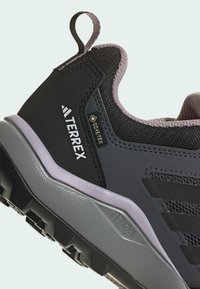 Chaussure de randonnée noire avec une tige texturée, étiquette Gore-Tex et une semelle en caoutchouc grise. Dispose d'une languette de traction et de trois rayures noires sur le côté.