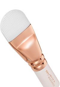 Applicateur en silicone blanc avec surface texturée, accents en métal doré et rose doré, et un manche blanc avec texte gravé.