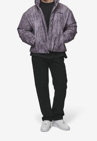 Gewatteerd paars jack met een gemarmerde textuur, ritssluiting aan de voorkant en hoge kraag. Gecombineerd met zwarte broek en witte sneakers.