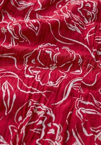 Tejido rojo con patrones florales blancos y líneas onduladas, con una superficie texturizada que resalta los pliegues y arrugas.