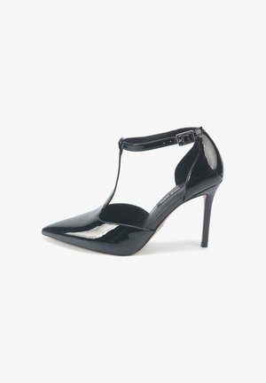 Zapato de tacón alto de charol negro con punta afilada, diseño de tira en T, hebilla en el tobillo y acabado brillante y suave.
