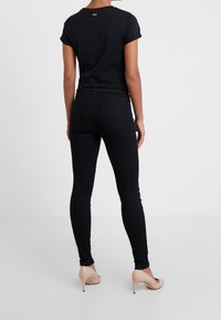 Un jean noir ajusté associé à un t-shirt noir à manches courtes, vu de dos. La tenue est complétée par des talons hauts nude.