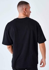 Camiseta negra de manga corta, hecha de algodón, con un corte holgado y cuello redondo. Textura suave y sin patrones ni impresiones visibles.