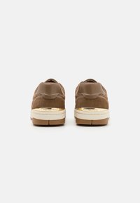 Paire de baskets marron avec semelles blanches et accents dorés, vue de dos sur un fond clair uni.