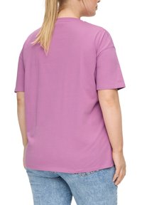 Paarse katoenen t-shirt met korte mouwen, relaxte pasvorm, ronde halslijn en subtiele stikdetails. Draag met blauwe spijkerbroek.
