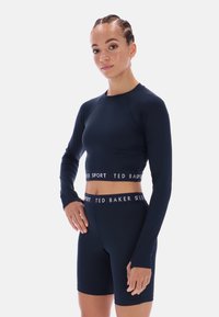 Tengerészkék hosszú ujjú sportos crop top és hozzáillő, magas derekú kerékpáros rövidnadrág, a derékrészen logós pánttal. Simaságot és rugalmasságot biztosító anyagból.