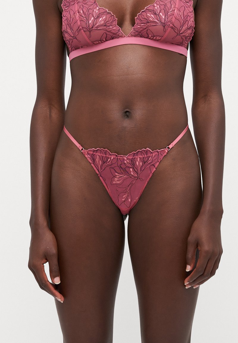 Bralette und Tanga-Set aus Spitze in Rosa mit Blumenmustern. Verstellbare Träger und gewellte Kanten an Bralette und Tanga.