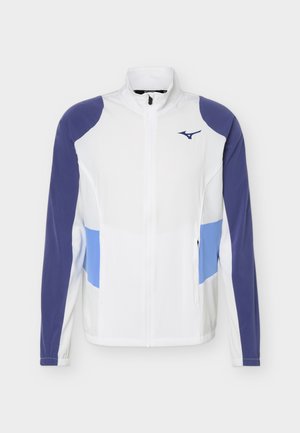 Fehér, teljes cipzáras dzseki lila ujjakkal, világoskék oldalpanelekkel, elasztikus mandzsettákkal és egy kis tengerészkék logóval a bal mellrészen.