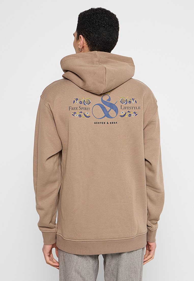 Bruine hoodie met een trekkoord in de capuchon, met een grafisch ontwerp in blauw en geel op de achterkant, geïnspireerd op natuur- en levensstijlthema's.