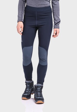 Marineblaue Leggings mit grauen Kniepatches und einem hohen Taillenbund, kombiniert mit schwarzen Wanderschuhen mit Schnürsenkeln und einer Gummisohle.