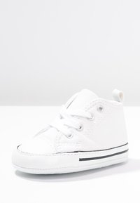 Białe trampki za kostkę z płótna, charakteryzujące się teksturowaną powierzchnią, okrągłym noskiem, białymi sznurowadłami i czarnym paskiem wzdłuż podeszwy.