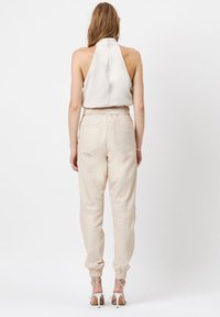 Witte haltertop met een gesloten rug, gecombineerd met beige tapered broeken met elastische manchetten en achterzakken. Zilveren enkelschoenen met bandjes.