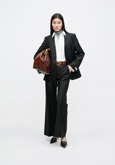 Μαύρο ταγέρ με φαρδιές παντελόνες, λευκό πουκάμισο, γκρίζα ψηλόμεση μπλούζα, καφέ δερμάτινη τσάντα και μαύρες μυτερές γόβες. Χρυσές λεπτομέρειες.