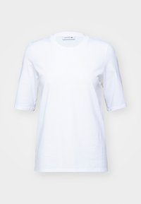White cotton t-shirt with short sleeves, round neckline, and an embossed Lacoste logo on the left chest. Smooth texture, straight cut.