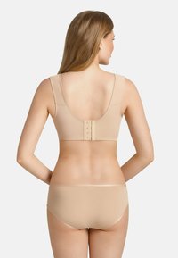 Soutien-gorge beige avec des bretelles larges, texture lisse et une fermeture à crochets au dos. Le bikini assorti présente un design simple.
