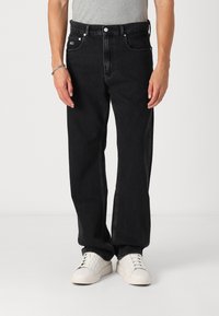 Jeans negri din denim cu o croială lejeră, design cu cinci buzunare și accesorii argintii. Purtați cu adidași albi.
