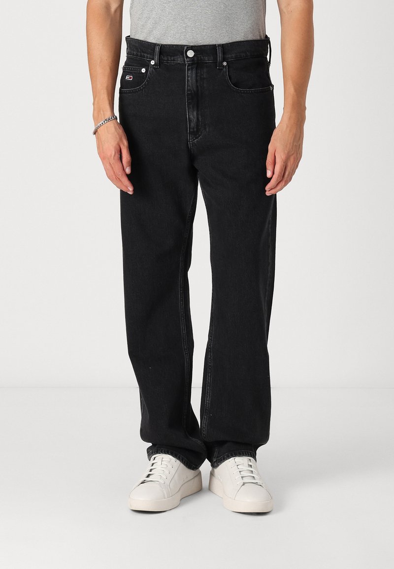 Jeans negri din denim cu o croială lejeră, design cu cinci buzunare și accesorii argintii. Purtați cu adidași albi.