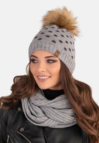 Grå strikket hue med ribbede design, prikket mønster og en faux fur pom-pom. Kombineret med et grå strikket tørklæde.