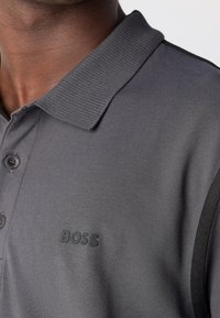Polo shirt en charbon avec un col à côtes texturé, deux boutons et un logo "BOSS" noir en relief sur le devant.