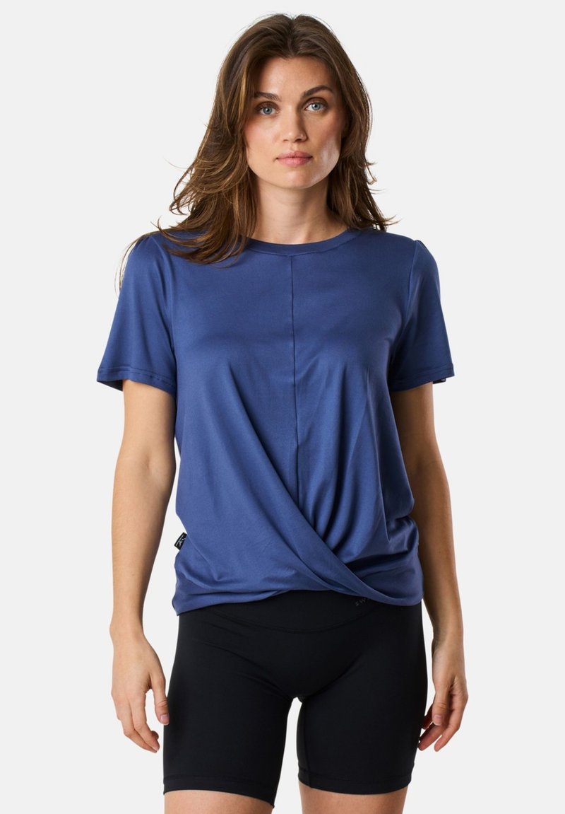 Blue short-sleeve t-shirt with a twist front design, made of soft material. It features a round neckline and a relaxed fit. Paired with black shorts.