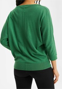 Grön stickad tröja med sjömanskrage, trekvartslånga ärmar och ribbat nederkant. Har en sömdetalj bak. Tillverkad med svarta byxor.