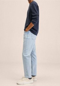 Jeans de mezclilla azul claro, corte relajado, combinados con un suéter de punto azul marino y zapatillas beige. Diseño sencillo, look casual.