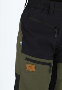 Czarne i oliwkowozielone spodnie cargo z kieszeniami na zamek, ozdobione szwedzką flagą oraz skórzaną łatą z napisem "Swedemount".