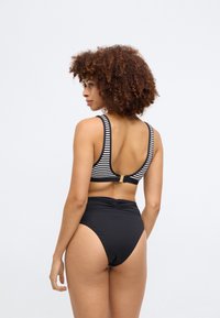 Fekete, magas derekú bikini alsó, csíkozott bralette-tel, mely hátul nyitott és arany fémházat tartalmaz. Simán tapintású, testhez álló kialakítás.