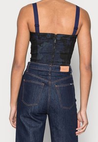 Top corsetto floreale nero con spalline blu navy, chiusura con cerniera sul retro; abbinato a jeans in denim scuro a vita alta con cuciture arancioni e tasche.