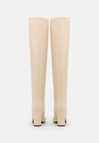 Botas beige hasta la rodilla hechas de cuero suave, con tacón de bloque y un diseño elegante con mínima costura y sin herrajes visibles.