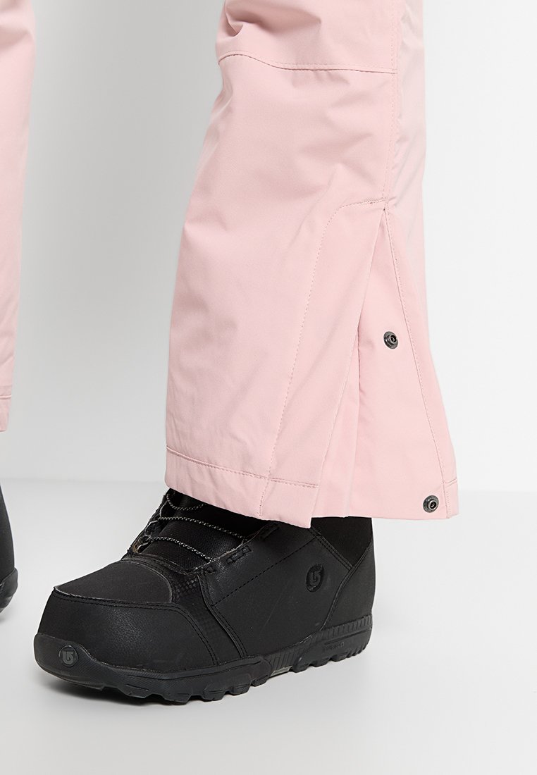Wodoodporne różowe spodnie narciarskie z zapięciem na zatrzaski u dołu, w połączeniu z czarnymi wodoodpornymi butami z teksturowanymi akcentami i wytrzymałymi podeszwami.